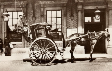 A stationary hansom cab and driver pulled by a horse
