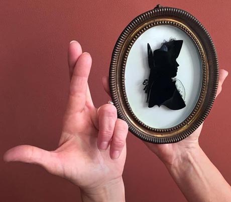 Photo of two hands, one with fingers crossed, the other holding a framed silhouette portrait