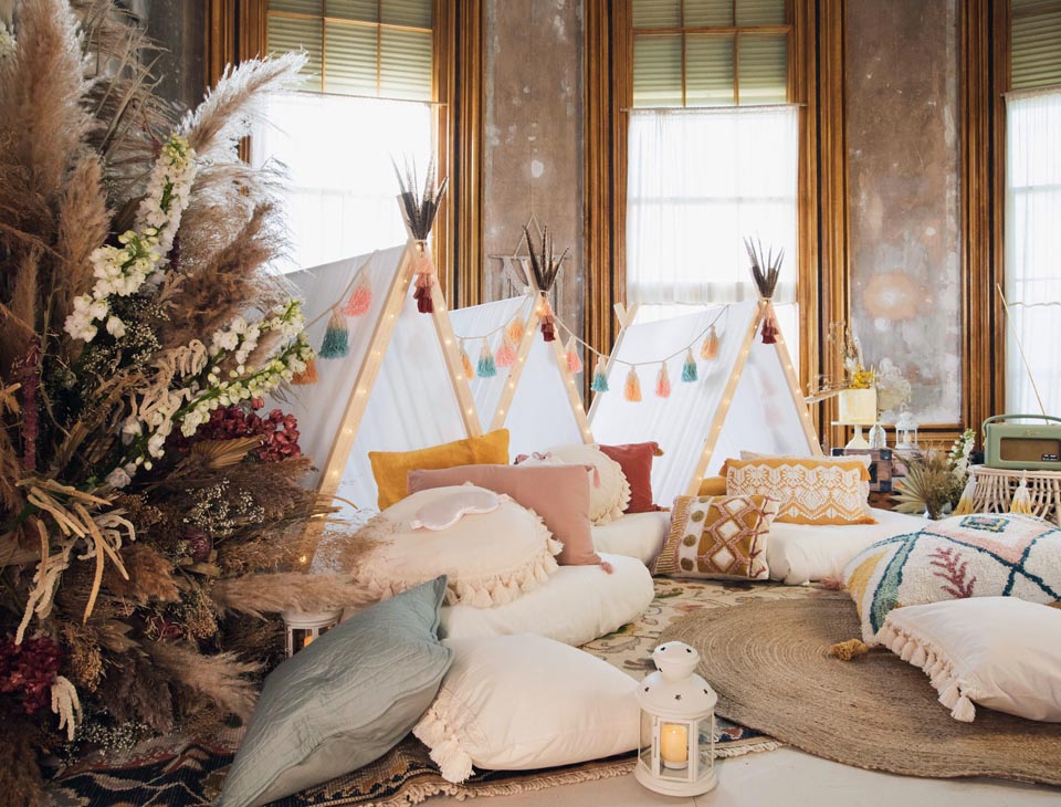 Photo showing a room decorated to resemble a camp site, with tents, cushions and foliage and 