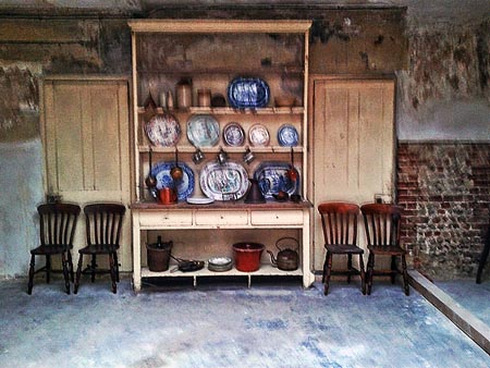 Photo of basement of number 10, showing old dresser with crockery and pans, flanked by two pairs of wooden chairs
