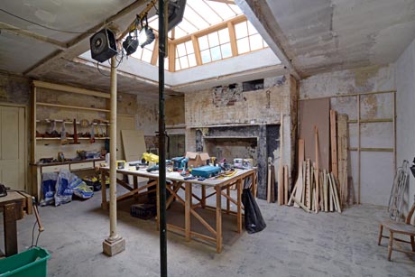 View of kitchen undergoing restoration showing fireplace and original shelves.