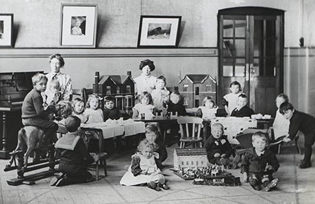 Black and white photo showing children and teachers in a schoolroom, circa 1910