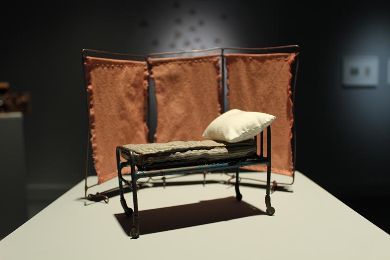 Miniature model of a tube-framed bed in front of a hospital screen.