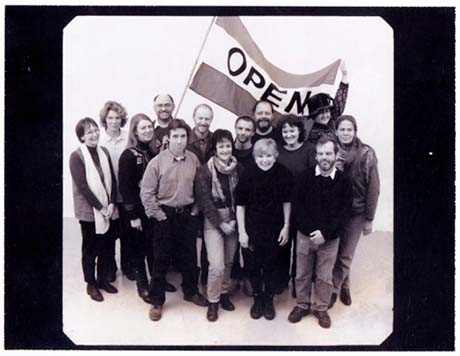 Black and white photo of a group of fourteen people, one carrying a flag with the word 'open'.
