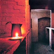 Photo of wine cellar, showing brick floor and stone shelves illuminated by candle light