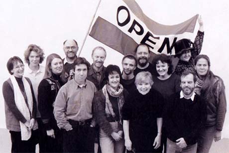 Black and white photo of a group of fourteen people, one carrying a flag with the word 'open'. 