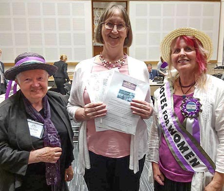 Photo of three women, one wearing a 'Votes for Women' sash and one holding a petition