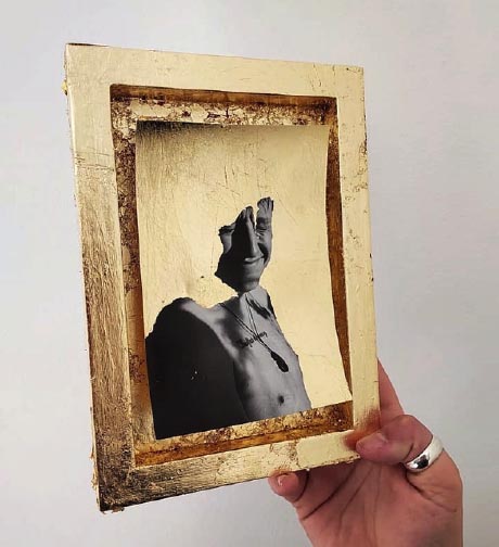 Photograph of a hand holding a gilded frame containing an image of a person