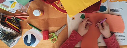 Overhead photo showing a child's hands holding coloured crayon and surrounded by art equipment
