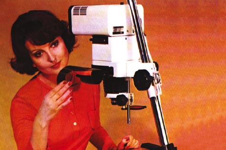 Photograph of a woman in a red top, loading a film roll into a white photographic enlarger