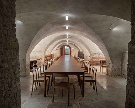 Photo showing a long dining table running the length of a restored cellar area with low vaulted ceiling.