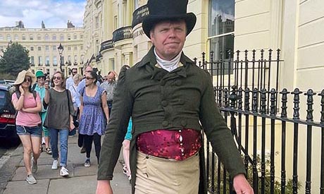 A man in Regency costume leading a tour group past a row of cream coloured town houses