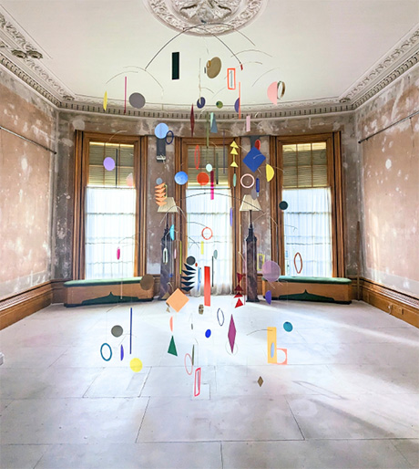Photo of a mobile comprising suspended coloured Perspex in a variety of geometreic shapes. It is hanging in the drwaing room of the Town House.