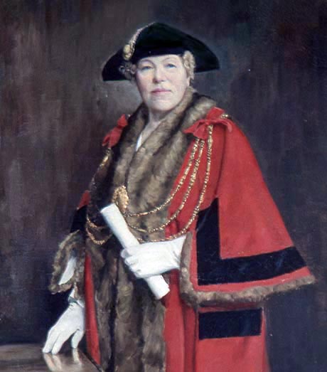 Painting of a lady wearing a red cloak, gold chains and a black cap, she is holding a scroll in her gloved hand.