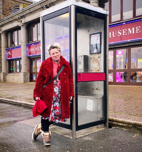 Photo of woman wearing a red coat and leaning on a modern, steel phone box