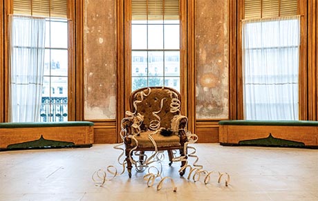 Photo of a Regency drawing room. In the centre of the floor is a deconstructed armchair and in the background there are three large windows