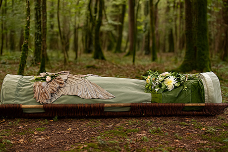 Photograph of a burial shroud and a wicker stretcher, on the ground in a woodland setting