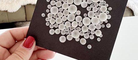 Photo of a hand holding a tiny artwork comprising white circles on a black background