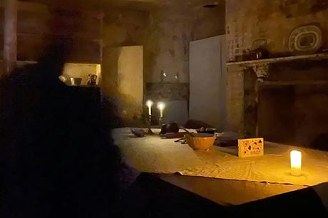 Photo of some kitchen utensils on a candle-lit table in a dark, bare room.
