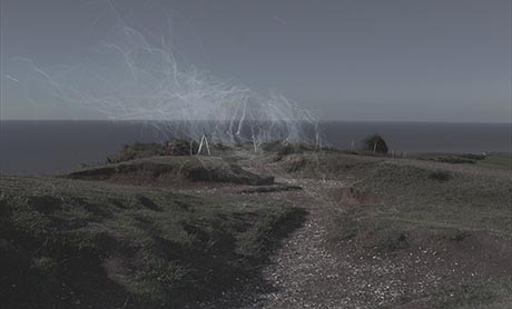 Landscape photo, taken looking across a headland and out to sea. There is a fence and whispy, smoke-like trails in the air.