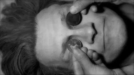 Black and white photo of a man's face in close up, with old pennies placed on his closed eyes.