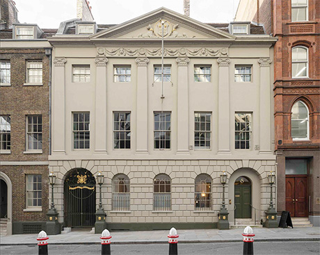 Photo of classically styled building: three storeys high, five windows wide, with cream stucco facade decorated with pilasters, rustication and a pediment over.